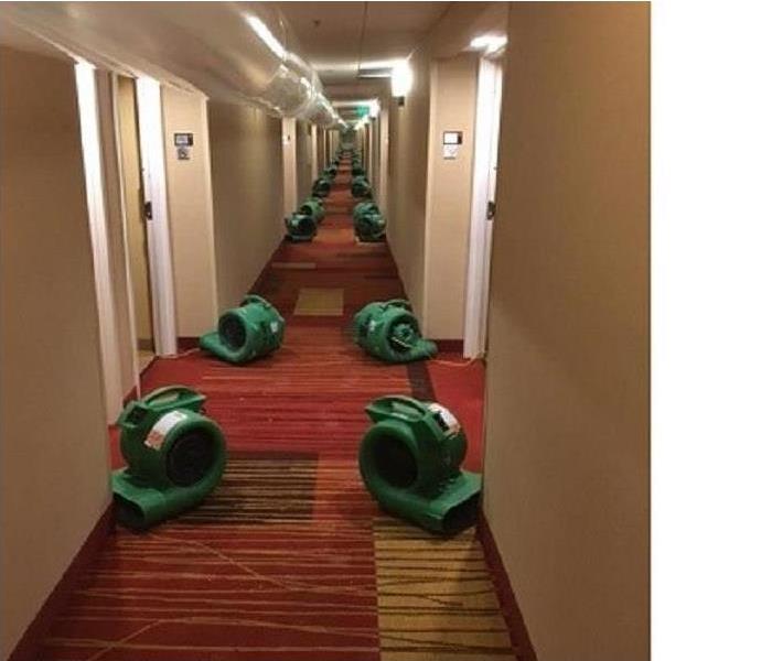 above is a lengthy conduit and below are two long rows of equipment in the carpeted hallway