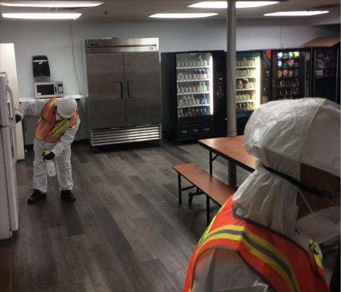 View of a fridge, drink dispensers, and Tyvek donned workers cleaning and wiping surfaces